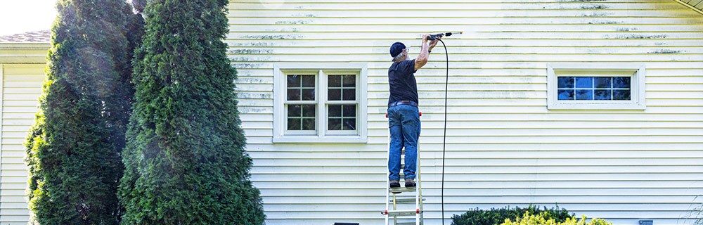 homeowner power washing their home's exterior while standing on a ladder