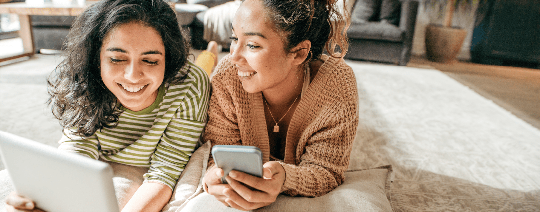 two girls laying on a rug looking at devices