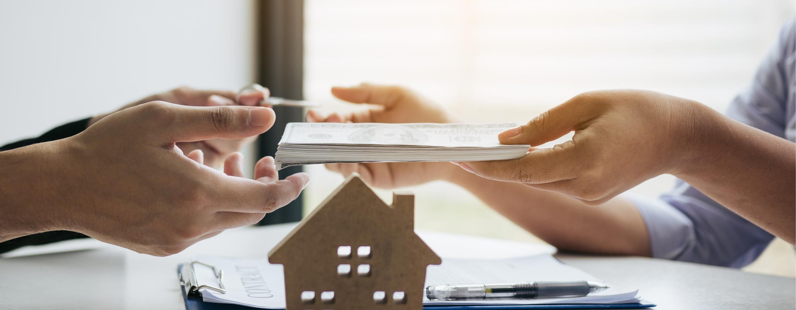 Image of hands passing money from one to another with a wooden cut out of a home in front of them