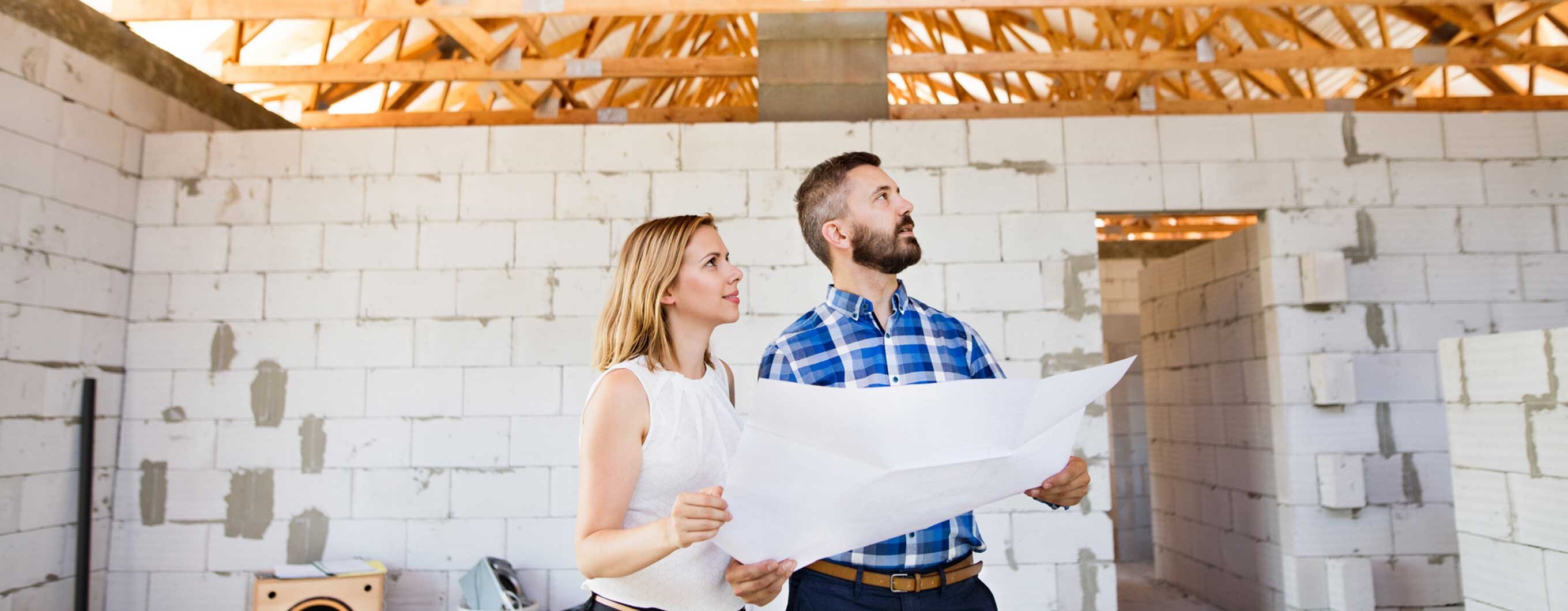 A man and a woman holding a blueprint inside a home under construction