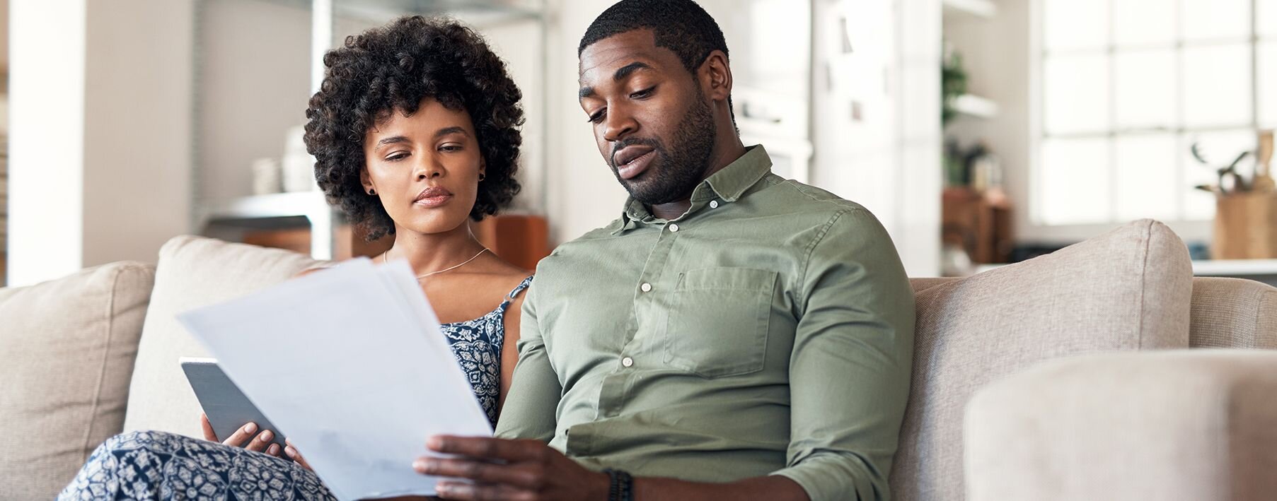 A couple sitting on a couch in their home looking at papers