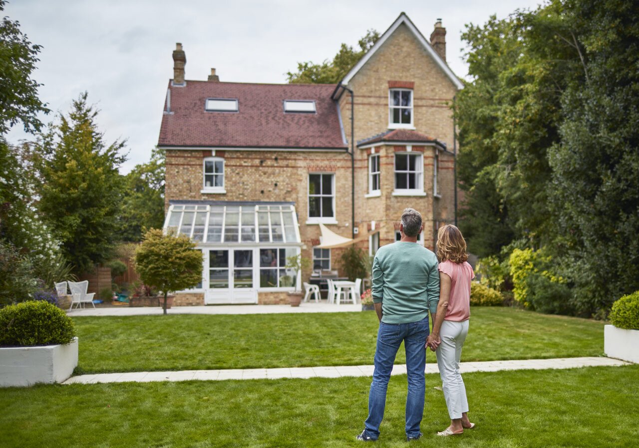 People stand looking at an older home, their backs to the camera.