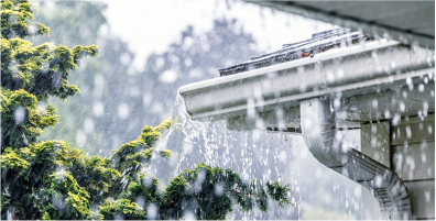 Image of the corner of a roof of a house during a rainstorm with water splashing out of a gutter
