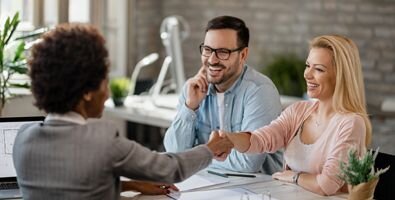 A woman and a man sit across a desk from another woman The two women are shaking hands