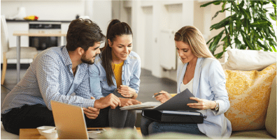 A man and a women sitting on a couch in an office, looking at paperwork with another woman