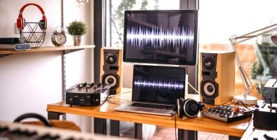 A desk with a laptop, a monitor, speakers and other music equipment