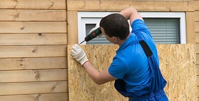 man drilling plywood over window