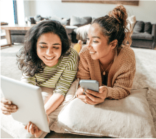two girls laying on a rug looking at devices