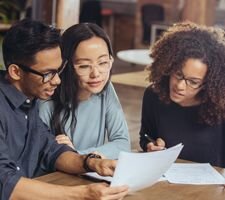 A man and woman looking at a piece of paper with another woman showing them something