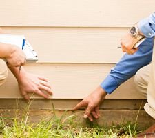 Two people squatting by a house pointing at a crack in the foundation