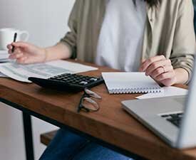 Image of a woman's torso and hands writing on a notebook and using a calculator