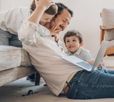 man leaning against couch on a laptop, his sons around him