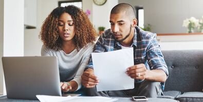 man and woman sitting on a couch looking at a laptop and papers