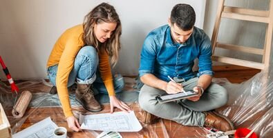 A young man and woman looking at construction plans in a room surrounded by painting materials