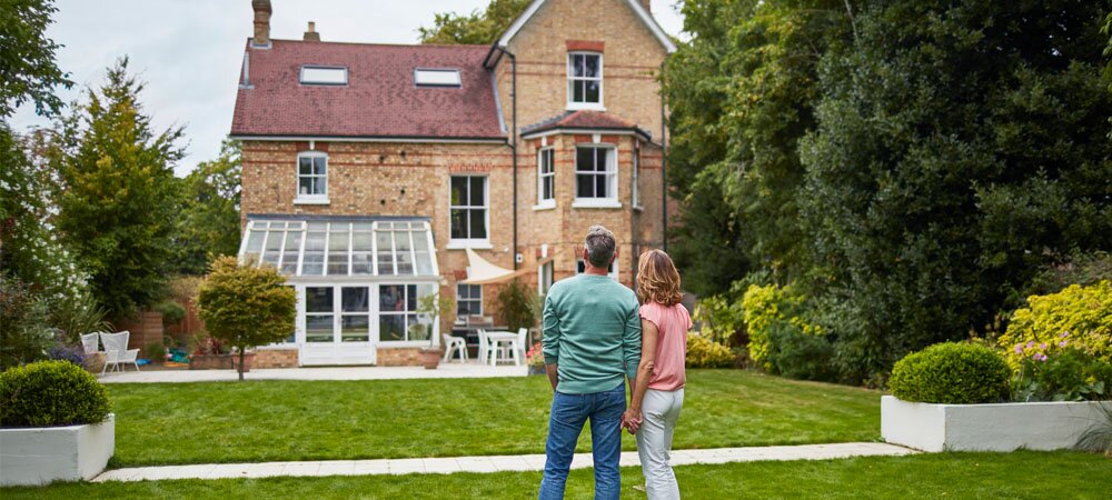 People stand looking at an older home, their backs to the camera.