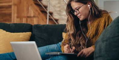 woman taking notes while watching a laptop